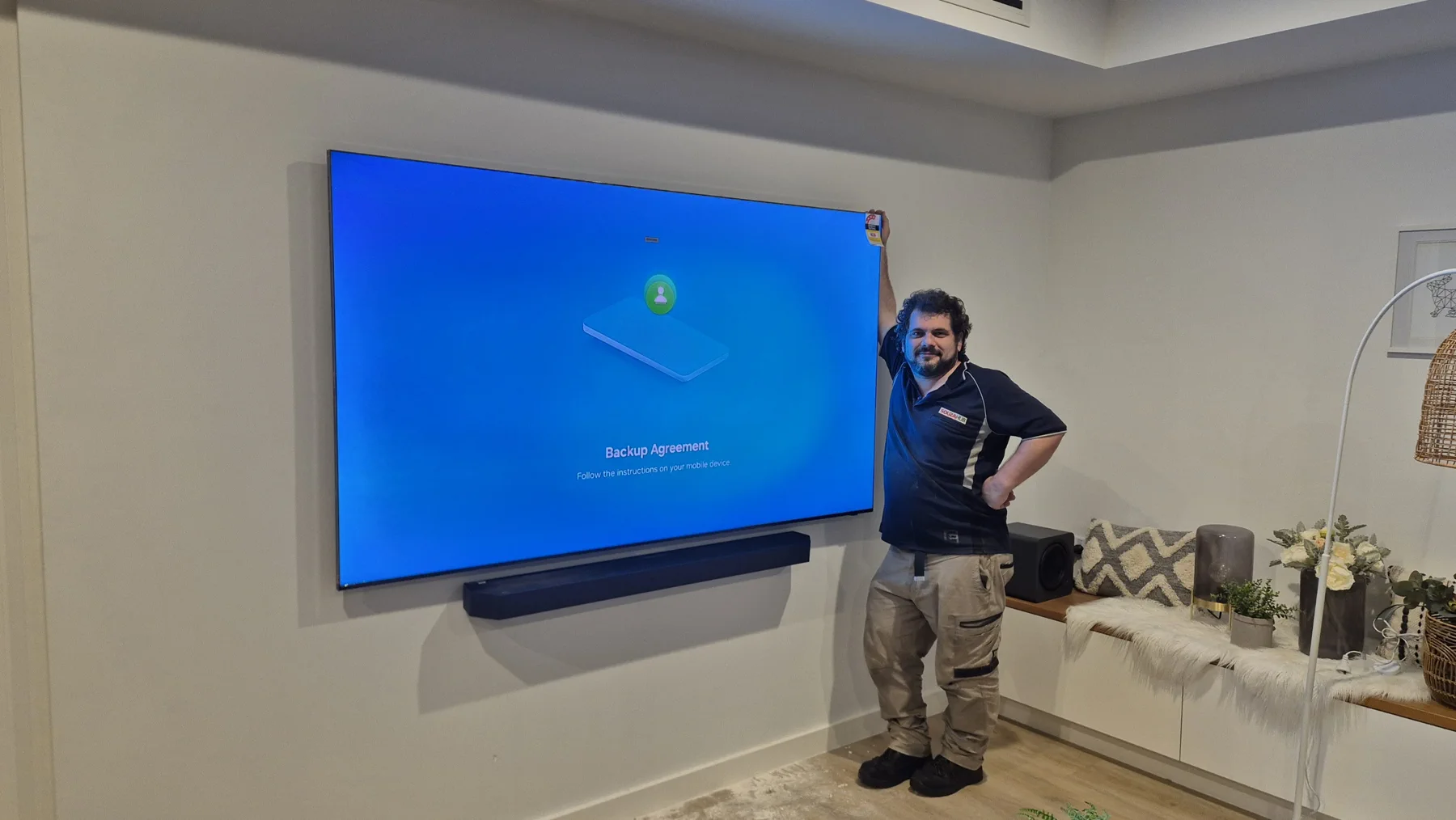 Danilo standing beside a large wall-mounted television, centred soundbar and separate subwoofer